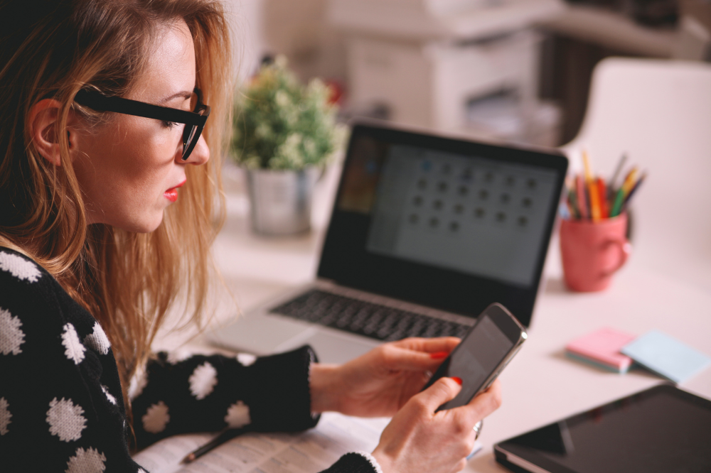 Woman juggling work tasks on phone and laptop.