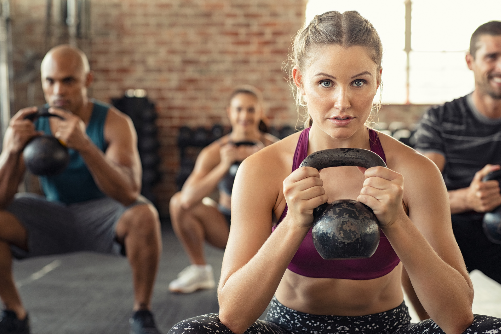 A group of focused individuals performing kettlebell squats in a gym, symbolizing strength, resilience, and teamwork in a fitness environment.