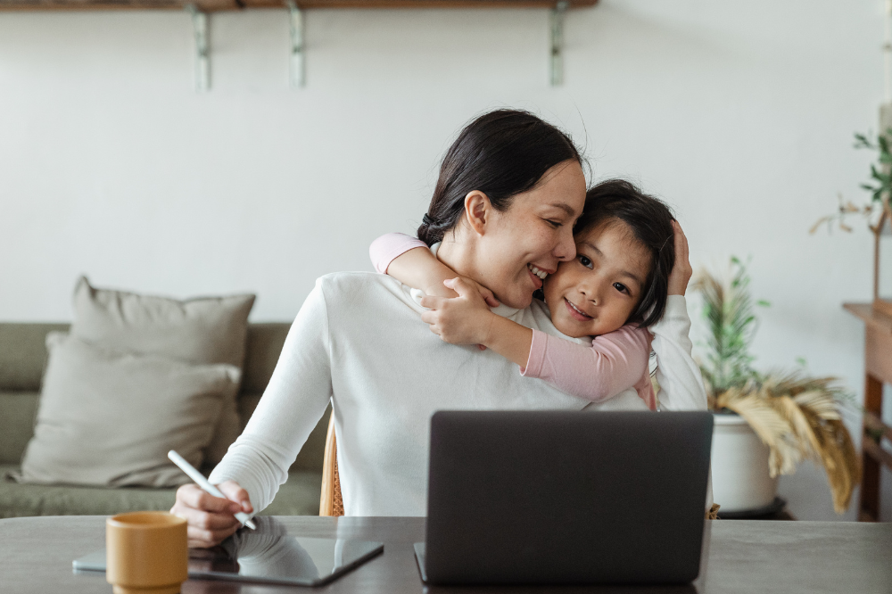 A mother working from home being hugged by child.