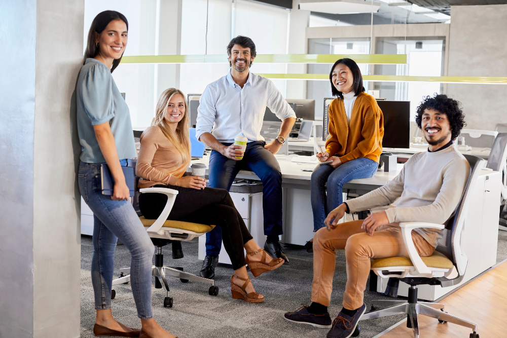 A group of smiling coworkers casually gathered in a modern office, representing a positive and collaborative work environment.